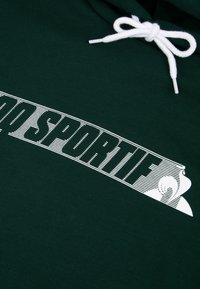 Sudadera verde con un diseño impreso en blanco que presenta el texto "SPORTIF" en negrita. Incluye un cordón blanco con puntas de plástico. Textura suave.