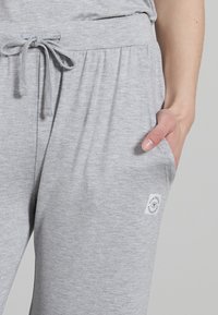 Grijze joggerbroek gemaakt van zachte stof, met een elastische tailleband en een aangetrokken koord, zijzakken en een klein wit logo-opbrengsel.
