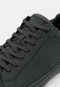 Black leather sneaker with textured surface, round laces, perforated accents on the tongue, and a smooth rubber sole.