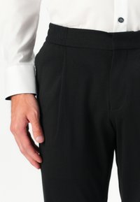Pantalones negros con una cinturilla elástica, con una textura suave y un diseño ajustado; se llevan con una camisa blanca de botones.