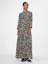 Vestido maxi com padrão de zebra preto e bege, mangas longas, frente abotoada e ajuste descontraído, combinado com sandálias de salto bloco pretas.