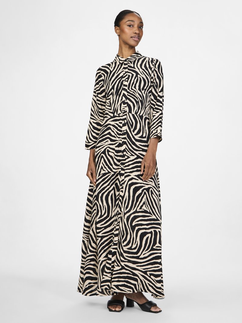 Vestido maxi com padrão de zebra preto e bege, mangas longas, frente abotoada e ajuste descontraído, combinado com sandálias de salto bloco pretas.