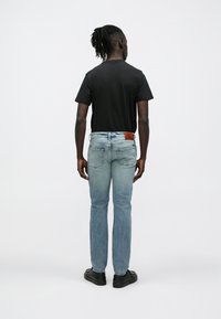 Čierne tričko s krátkym rukávom v kombinácii so svetlomodrými džínsami, s hnedou koženou značkou na opasku a čiernymi topánkami. Modelka je zobrazená zozadu.