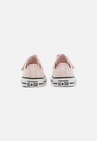 Zapatillas de lona bajas en color rosa con suelas de goma blanca, detalles de raya negra y la marca 'Converse All-Star' en negro en el talón.