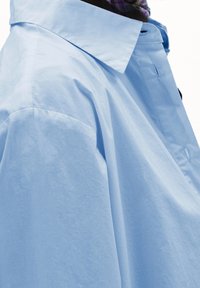 Light blue oversized shirt, made of soft fabric, featuring a wide collar and visible buttons on the side, showcasing a smooth texture.
