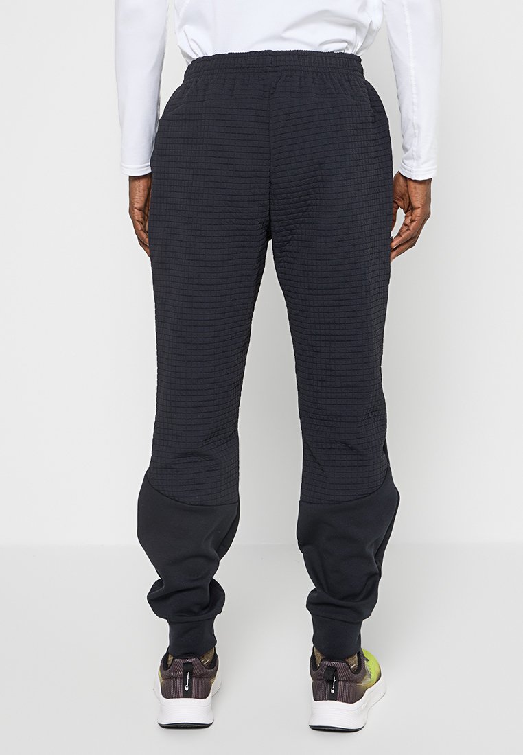 Pantalons de survêtement noirs avec un motif en grille texturé sur les sections supérieures et des sections inférieures lisses. Ils présentent une taille élastique et des poignets fuselés.