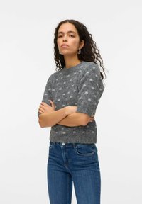 Grå kortärmad tröja med ett texturerat mönster av ljusgrå prickar, rundad halsringning och en figursydd design. Kombinerad med blå jeans.
