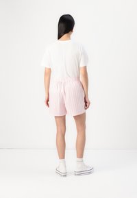 Hvit t-skjorte kombinert med rosa stripete shorts. Shortsene har elastisk midje og en avslappet passform. Hvite høyhælte sneakers fullfører antrekket.