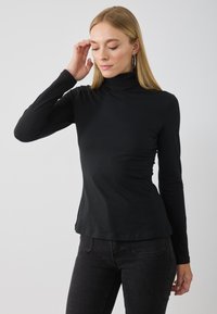 Must mustaga turtleneck särk, millel on pikad varrukad ja mis on valmistatud pehmest kangast. Kitsa lõikega disain, sile tekstuur ja kaardus alläär.