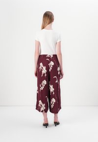 Hvit kortermet topp kombinert med bordeaux vide bukser med blomsterdesign i krem, med elastisk midje og ankel-lengde kant.