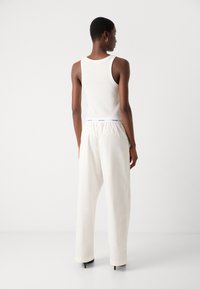 White tank top and loose-fitting, cream trousers with an elastic waistband. Black high-heeled shoes, minimalistic design, smooth texture.