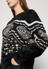 Maglione lavorato a maglia in bianco e nero con motivi astratti, polsini fluff texture, e una scollatura ampia, con una vestibilità rilassata e maniche lunghe.