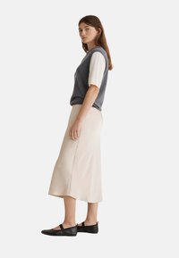 Suéter gris sin mangas con cortas mangas crema, combinado con una falda midi beige y zapatos planos negros. Tejido suave y diseño simple.