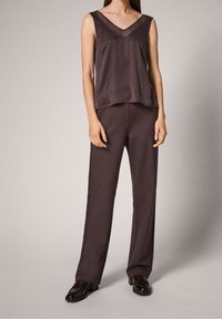 Haut sans manches en satin avec un décolleté en V de couleur violet foncé, associé à un pantalon large assorti. Les chaussures sont noires avec une finition texturée.