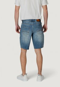 Shorts de mezclilla con un lavado azul claro, de corte recto, cinco bolsillos y costuras en contraste. Combinados con zapatillas blancas y una camiseta básica.