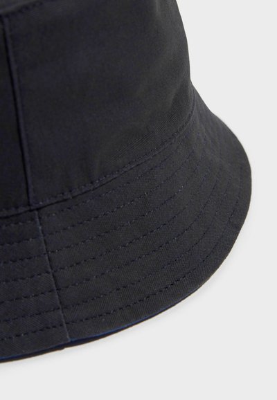 Cappello a secchiello nero, realizzato in tessuto testurizzato, con una visiera larga e leggermente morbida e dettagli di cucitura visibili sulla corona e sui bordi della visiera.