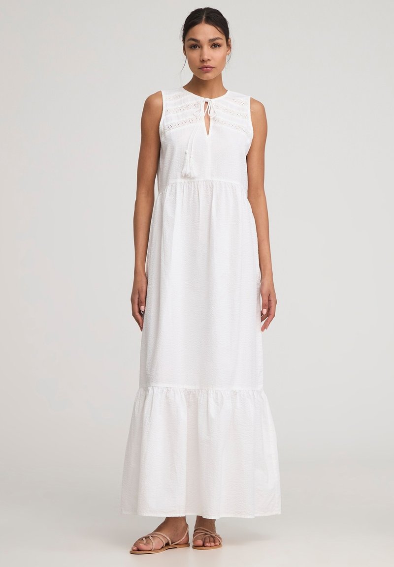 Abito maxi bianco con tessuto strutturato, design senza maniche, scollatura a chiave e orlo a strati. Accentuato da un nodo e frange.