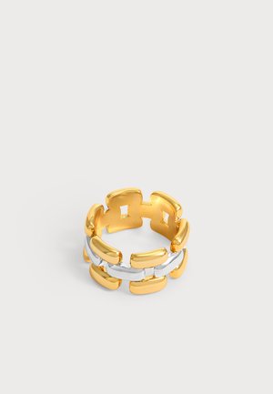Anillo de eslabones de cadena rectangulares entrelazados en oro y plata con parte trasera abierta sobre un fondo gris claro.