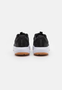 Zapatillas deportivas negras con parte superior texturizada, suela blanca y tracción de goma. Presentan una lengüeta y un logo en el talón.