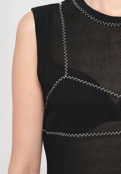 Haut en tricot noir avec un col rond et sans manches, agrémenté de surpiqûres en zigzag blanches contrastantes sur le tissu.