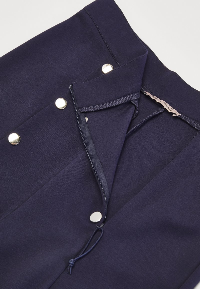 Navy blue fabric with a smooth texture, featuring silver snap buttons and a drawstring. The garment has a clean-cut design and finished edges.