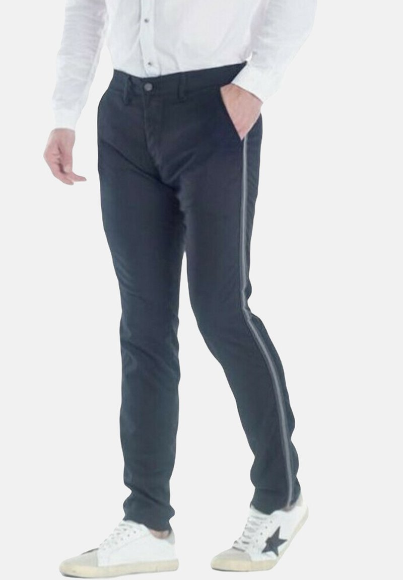 Pantaloni neri con una vestibilità slim, caratterizzati da una striscia laterale. Indossati con sneakers bianche, che mettono in risalto una textura simile al cotone.