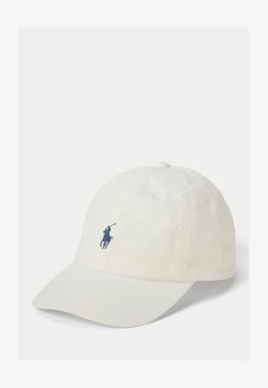 Valge pesapalli nokamüts kaardus nokaga ja sinise tikitud polo mängija logoga esikeskmes.