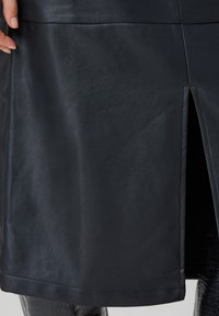 Jupe en cuir noir avec une texture lisse et une fente à l'avant. Présente un ourlet net et des détails de couture sur le côté.