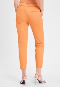 Oranje, slim-fit broeken met een gladde textuur, voorzien van twee achterzakken en cropped hems, gecombineerd met zilveren hoge hakken sandalen.