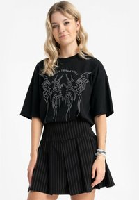 Czarny, oversize'owy t-shirt z srebrnym nadrukiem pająka i napisem, w połączeniu z czarną, prążkowaną spódnicą. Charakteryzuje się luźnym fasonem i miękkim materiałem.