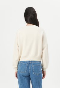 Felpa in cotone con vestibilità rilassata, maniche raglan e orlo a coste, abbinata a jeans blu a vita alta con tasche posteriori.