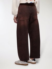 Jeans a gamba larga di colore marrone scuro in denim, con tasche posteriori, tessitura media e una finitura leggermente sbiadita vicino all'orlo.