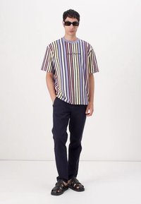 Striped short-sleeve shirt in pastel colors, featuring horizontal lines. Paired with dark pants and black sandals. Minimal accessories.