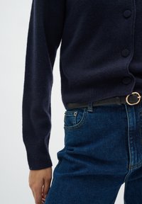 Marinblå stickad cardigan med runda knappar, i kombination med blå denimjeans med sömmar och ett svart bälte med ett guldspänne.