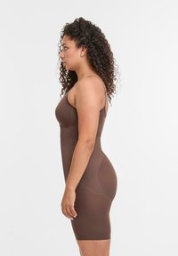Abito bodycon marrone con spalline sottili, design aderente, lunghezza al ginocchio, texture liscia e un leggero lucido. Nessun motivo o accessorio visibile.