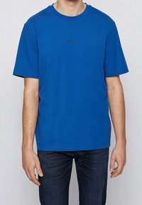 Blå bomulls t-shirt med rund halsringning, korta ärmar och en liten svart logotyp på bröstet. Kombination med mörk denimjeans.