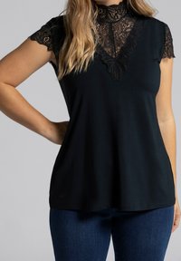 Haut noir avec un col en dentelle et des manches courtes, présentant des détails en dentelle complexe autour du col. Tissu doux, coupe décontractée.