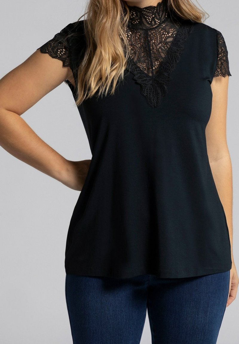 Haut noir avec un col en dentelle et des manches courtes, présentant des détails en dentelle complexe autour du col. Tissu doux, coupe décontractée.