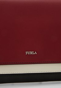 Section de sac à main en cuir rouge, blanc et noir avec le logo Furla en argent centré sur le panneau en cuir rouge.