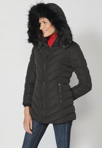 Geacă puffer neagră cu glugă căptușită cu blană sintetică, model cu romburi, buzunare laterale cu fermoar și siluetă ajustată.