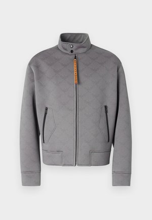 Pelēka zipa jaka ar augstu apkakli, ar reljefu rakstu un oranžiem aksesuāriem. Ietver divas iešūtas sānu kabatas ar rāvējslēdzējiem un taisnu griezumu.