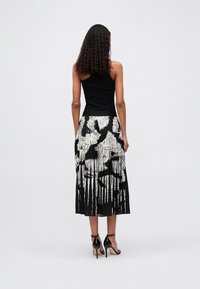 Μαύρο αμάνικο τοπ συνδυασμένο με πλισέ μίντι φο�ύστα που διαθέτει λευκό μοτίβο φύλλων, με μαύρες γραμμές. Φοριέται με μαύρες γόβες.