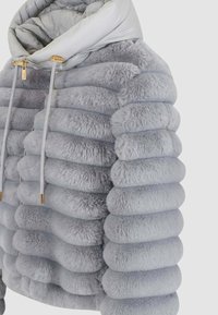 Giacca piuma in grigio chiaro in pelliccia sintetica con design trapuntato, caratterizzata da una consistenza soffice, un cappuccio oversize e dettagli in hardware dorato.