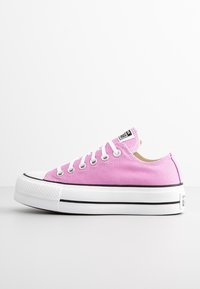 Låg topp rosa canvas sneakers med vit gummisula, vita snören, silverfärgade öglor och svart randdetalj på sulan.
