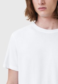 T-shirt bianco a maniche corte con scollatura rotonda. Texture liscia, design semplice e bordi puliti. Il tessuto appare leggero e traspirante.