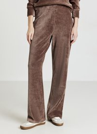 Pantaloni a gamba larga in velluto a coste marrone con texture a costine verticali, caratterizzati da una vestibilità comoda e una cintura liscia. Abbinati a sneaker bianche.