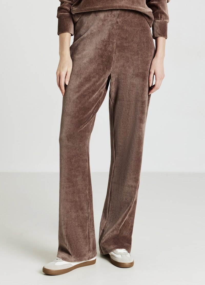 Pantaloni a gamba larga in velluto a coste marrone con texture a costine verticali, caratterizzati da una vestibilità comoda e una cintura liscia. Abbinati a sneaker bianche.