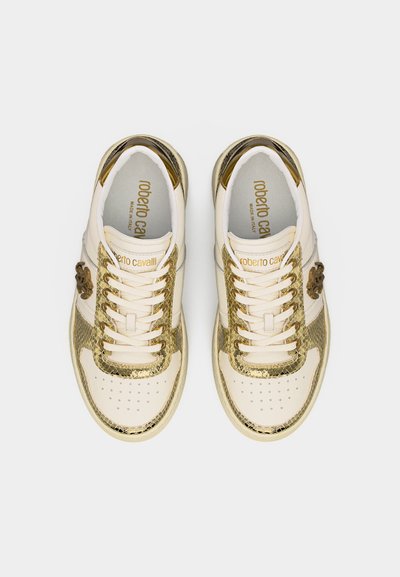 Paire de baskets crème et or métallique avec lacets, zone perforée à l'avant, et marquage "Roberto Cavalli" à l'intérieur et sur la languette.