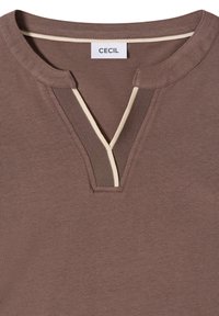 T-shirt marron à col rond avec une encoche en forme de V et un bord contrastant beige et marron foncé le long du col, étiqueté "CECIL".
