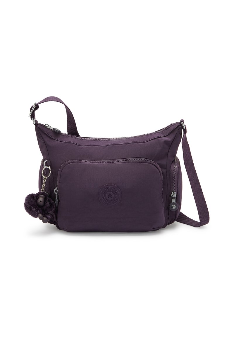 Lilla polyester crossover taske med en blød tekstur, der har en frontlomme med lynlås, et logo patch og en dekorativ pom-pom nøglekæde.